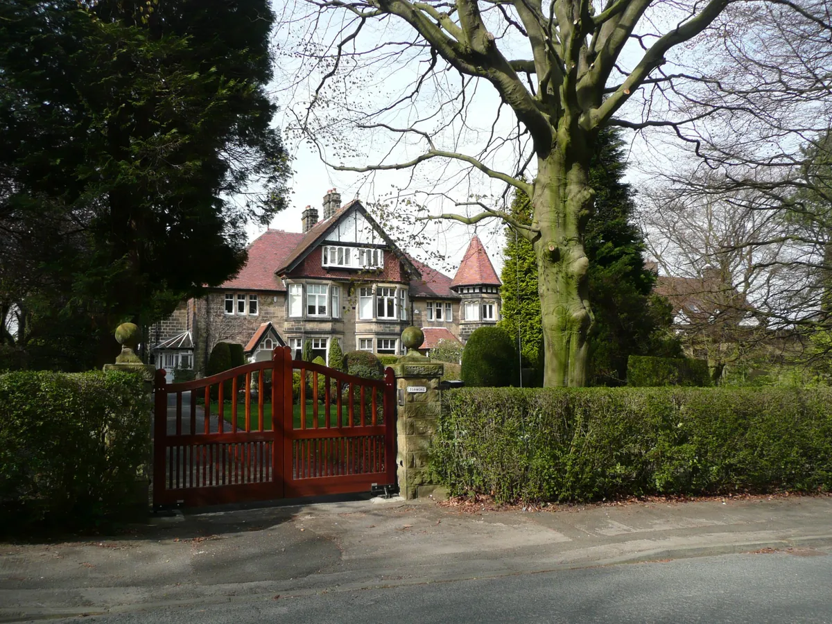 A large gabled stone house behind a wooden gate and a tall tree on Grove Road, Ilkley