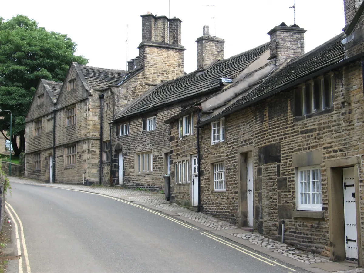 Old gritstone cottages beside a cobbled pavement on Church Street South in Old Glossop