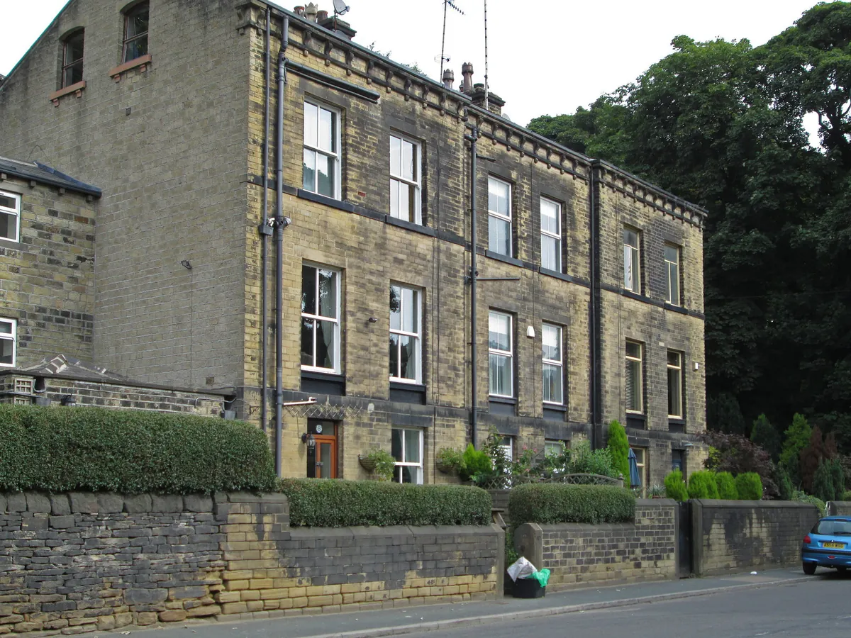 A tall stone terrace behind low walls and hedges on Rochdale Road, Sowerby Bridge