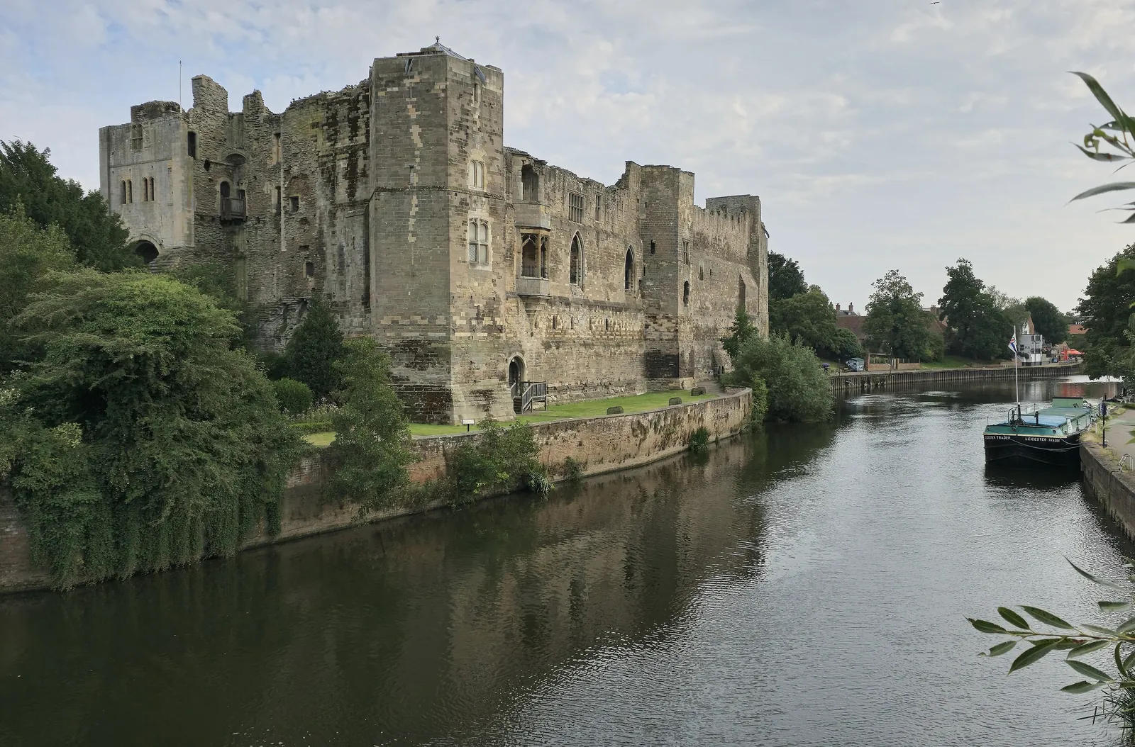 The ruined walls of Newark Castle rising above the River Trent, with a boat moored opposite