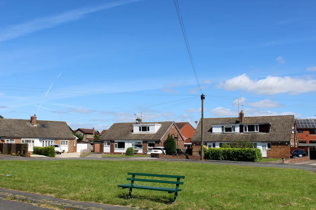 Brick bungalows around a green with a bench on Moor Lane, Sherburn in Elmet
