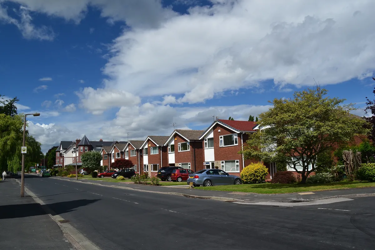 A row of red-brick houses with front lawns on Dairyground Road in Bramhall, under a blue sky